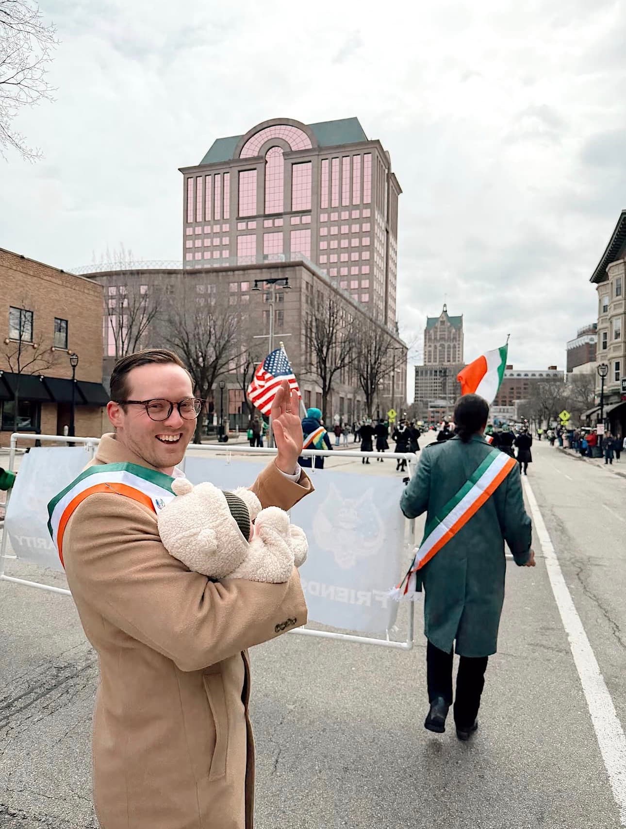 AOH Milwaukee brother in Irish sash waving during the St. Patrick's Day Parade with the Milwaukee skyline in the background